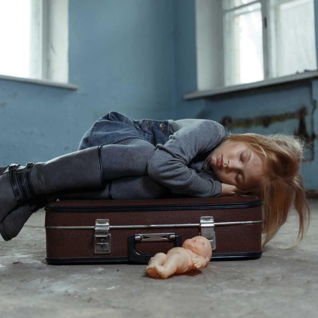The helpless orphan girl lies curled up on her clothes-filled luggage