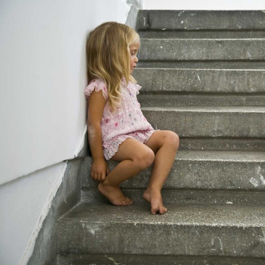 The orphan girl is looking at the edge of the stairs with her head against the wall