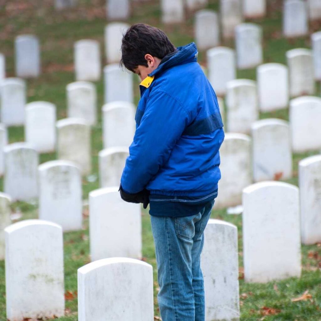 The orphaned boy is crying standing next to his parents' graves in the cemetery