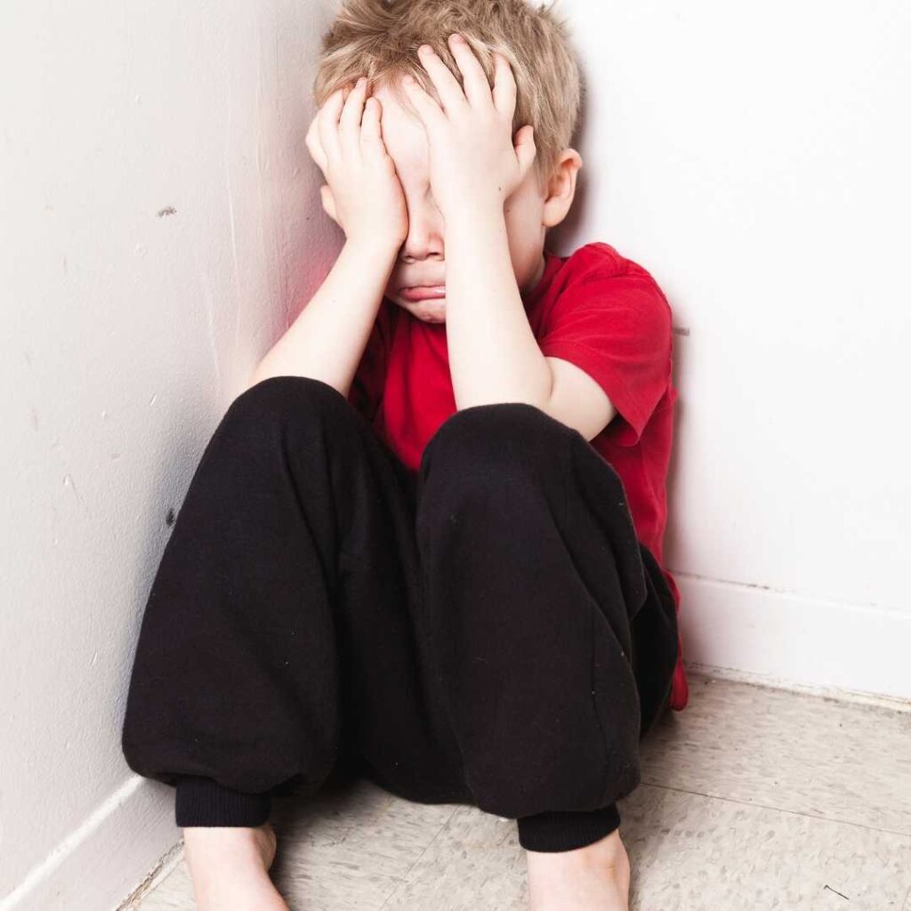 The orphaned boy, leaning against the wall, covers his face with both hands and cries