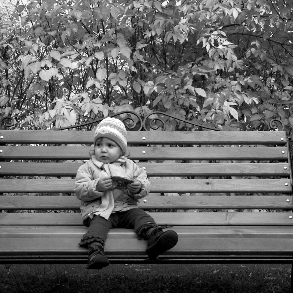 The orphaned child is sitting alone on a park bench in severe winter