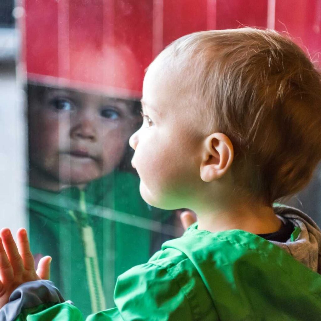 The orphaned child stares blankly at the horizon through the window glass