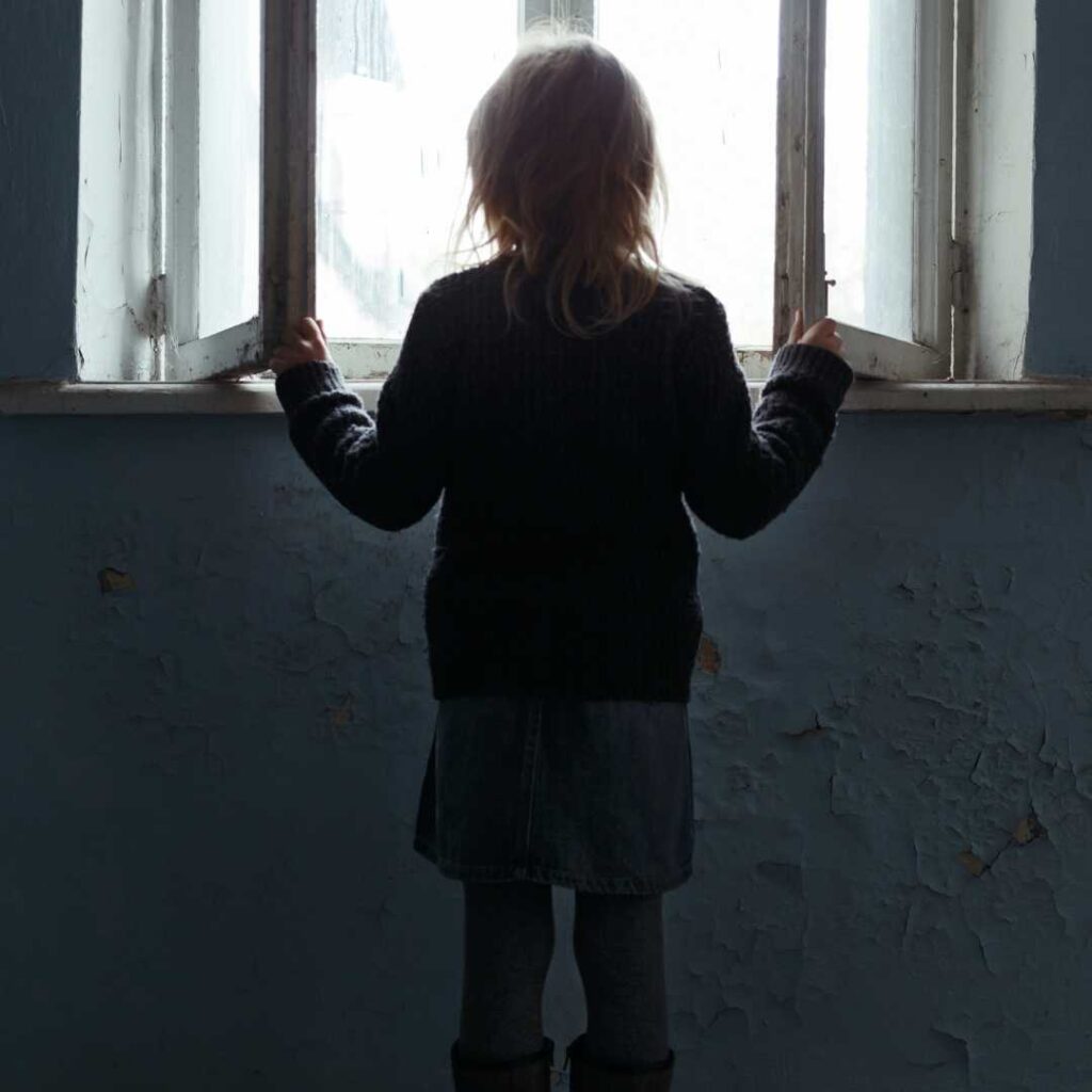 The orphaned girls stares blankly at the horizon through the window