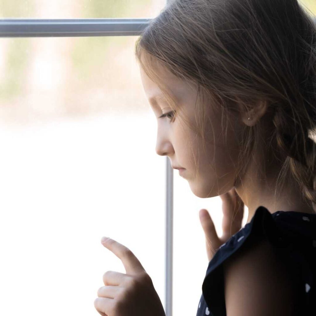 This lonely orphan girl is looking at the street below, holding her head against the glass window