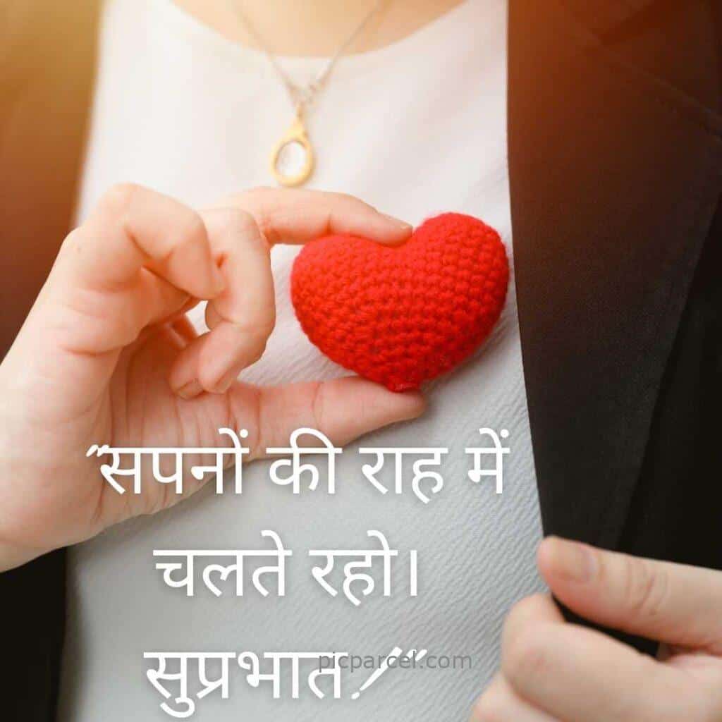 A person holds a small red knitted heart near their chest. Hindi text overlay reads सपनों की राह में चलते रहो। सुप्रभात। good morning quotes in hindi